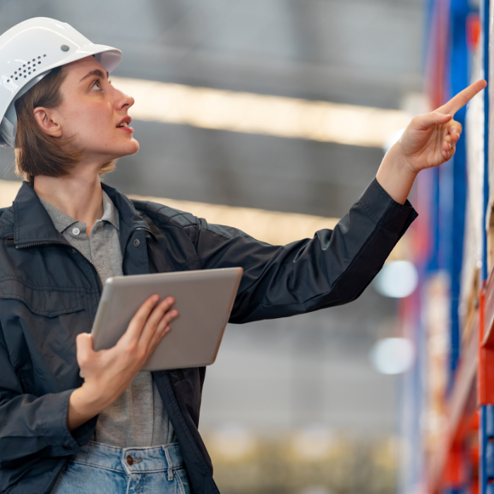 Woman with hardhat and tablet looking at finished goods stacked in boxes