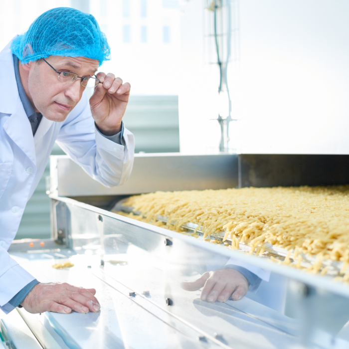 man in hairnet examines pasta as it is being manufactured