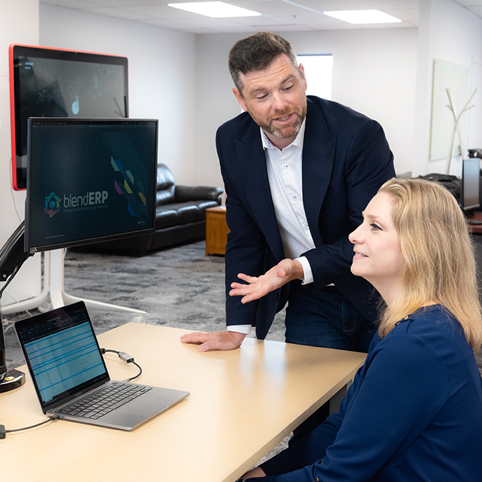 Sales Manager LP presenting to potential Health & Beauty Client who looks towards the presentation screens. Blend ERP and NetSuite can be seen on the two screens