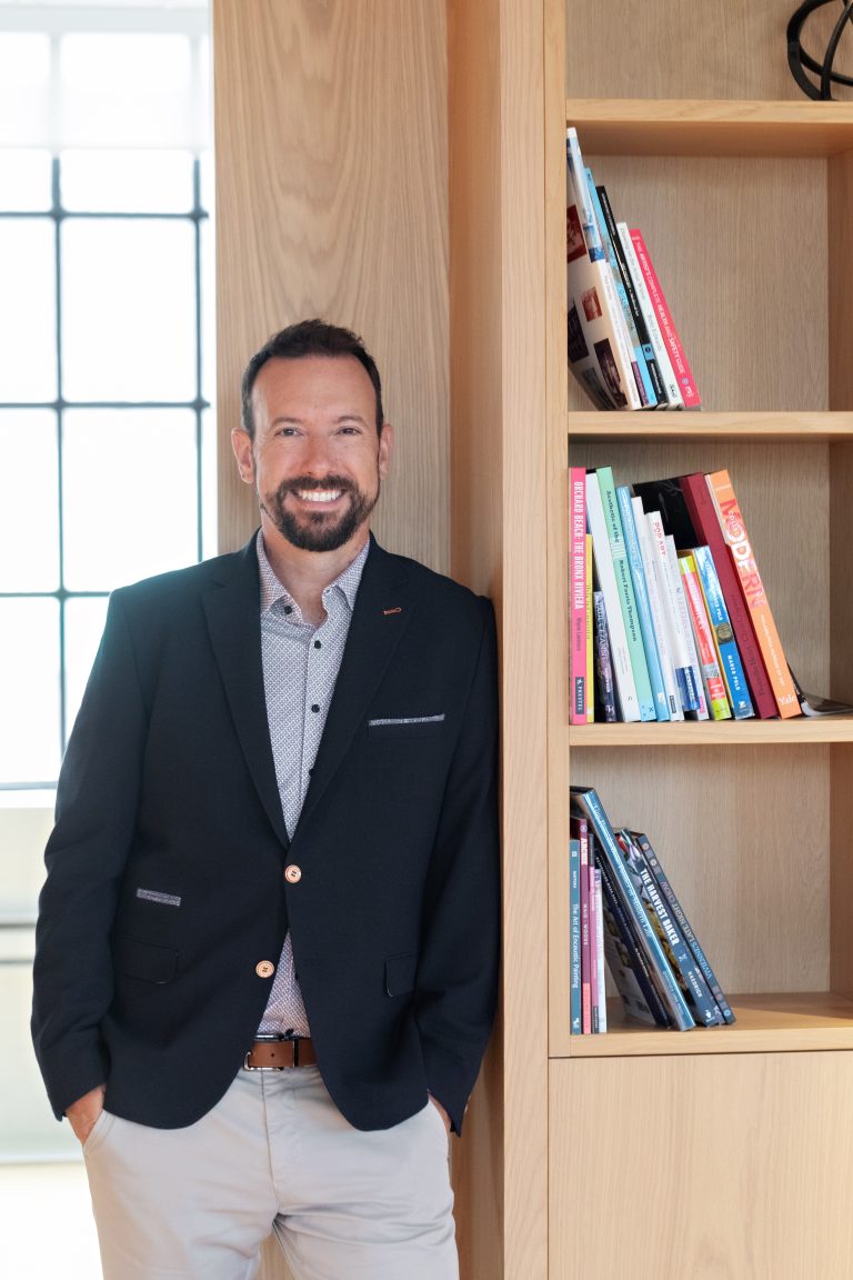 Michael Cairns, Co founder of Blend ERP smiling at camera, leaning on bookshelf with window behind